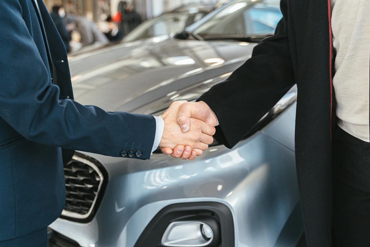 Poignée de main devant un véhicule scellant l'accord de rachat entre un client et le rachateur